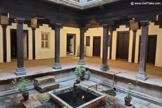 an old building with columns and water in the center, surrounded by potted plants