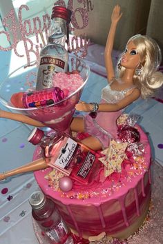 a barbie doll sitting on top of a cake with pink icing and sprinkles