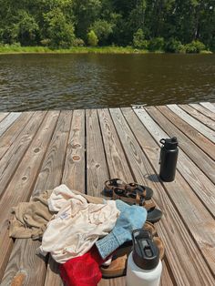 clothes, water bottle and flip flops sitting on a wooden dock next to a lake