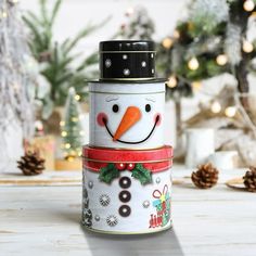 a stack of tin canisters with a snowman on top and christmas decorations in the background