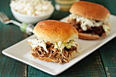 a pulled pork sandwich with coleslaw and french fries on a plate next to it