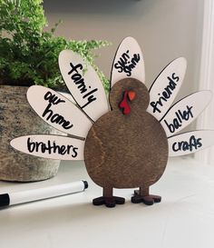 a wooden turkey with writing on it sitting next to a pen and potted plant