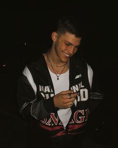 a man standing in the dark looking at his cell phone while wearing a black and white jacket