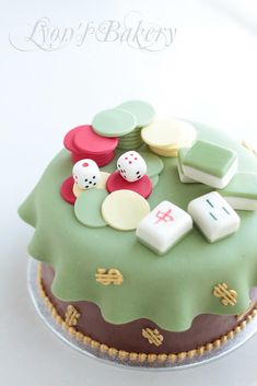 a green cake with dice and other items on it's top layer, sitting on a table