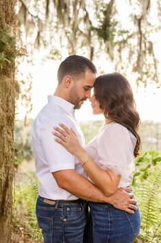 a man and woman standing next to each other in front of trees with moss growing on them