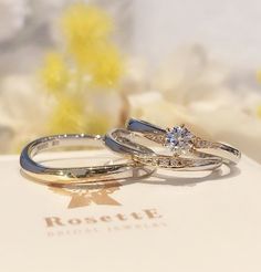 two gold wedding rings sitting on top of a white box with flowers in the background