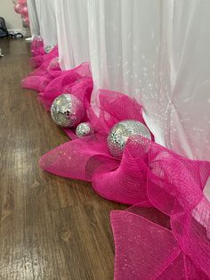 pink and silver balls are lined up on the floor in front of white drapes