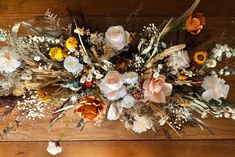 an arrangement of flowers and grasses on a wooden table with white, orange, yellow and pink blooms