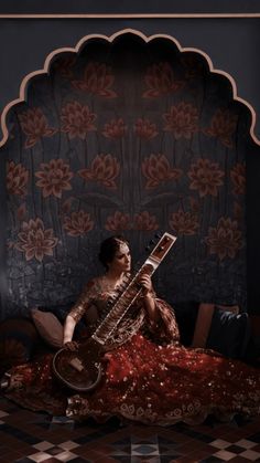 a woman sitting on top of a bed next to a wall with an instrument in her hand