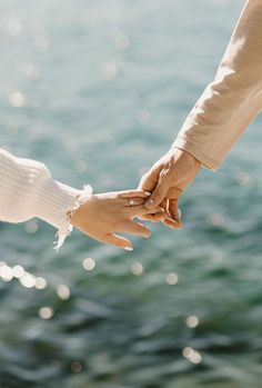 two people holding hands over water with sunlight reflecting off the water in the back ground