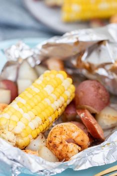 an aluminum foil container filled with corn, potatoes and shrimp on top of a blue plate