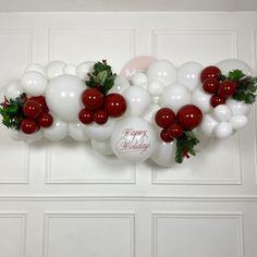 white and red balloons are hanging on the wall with greenery, holly leaves and berries