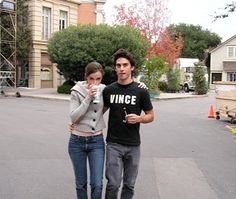 a man and woman standing in the middle of an empty parking lot, one holding a drink