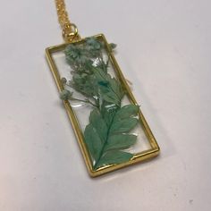 Dried flowers encased in resin surrounded by a goldtone rectangular bezel pendant on a 16" goldtone chain. Sage Green Necklace, Gold Resin Flower Pendant Necklace, Nature-inspired Green Necklace With Large Pendant, Unique Green Resin Necklace, Nature-inspired Green Necklace With Pressed Flowers, Green Pressed Flower Round Pendant Jewelry, Sage Green Flowers, How To Dry Sage, Dance Necklace