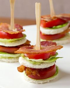 small sandwiches with bacon, lettuce and tomato on a white plate topped with toothpicks