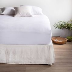 a bed with white linens and pillows on top of it next to a wooden bowl