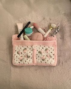 a pink crocheted purse with various items in it sitting on a white blanket