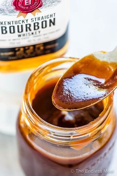 a spoon full of brown liquid next to a bottle of bourbon on a white table