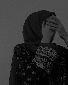 a woman in a headscarf covers her face with her hands as she stands against a wall