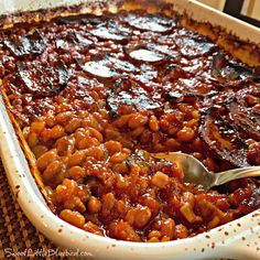 a casserole dish filled with baked beans and topped with a spoon in it