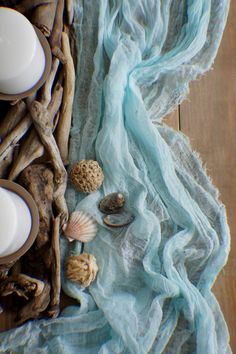 seashells and candles are sitting on a blue cloth next to some driftwood