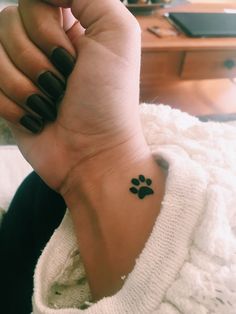 a woman's wrist with a small paw tattoo on it