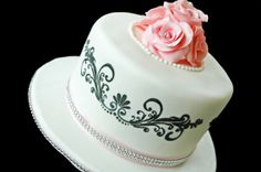 a white cake with pink flowers on top and black trim around the edges, sitting on a plate