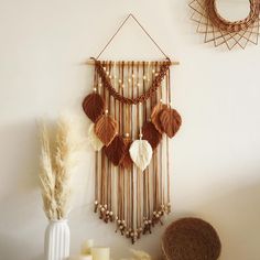 a wall hanging with beads and tassels on it next to a white vase