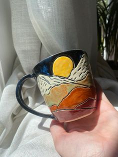 a hand holding a coffee cup with an image of the sun and mountains on it