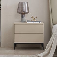 a nightstand with a lamp on top of it next to a bed and a white blanket