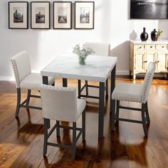 a dining room table and chairs with pictures on the wall above it, along with a vase filled with flowers