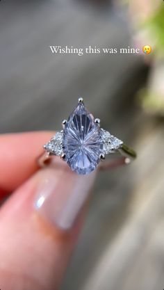 a person holding a ring with a blue stone in it's center and two white diamonds around the band