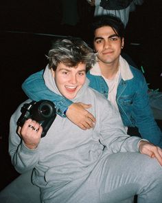 two young men sitting next to each other and one is taking a selfie with his camera