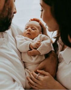 a man and woman holding a baby in their arms while they look at each other