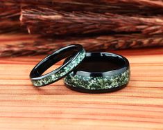 two wedding bands with green and black flowers inlayed to them on a wooden surface