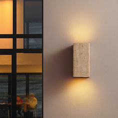 a couple of people sitting at a table in front of a wall mounted light that is on the side of a building