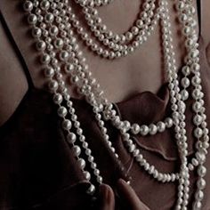 a close up of a person wearing pearls on their necklaces and holding something in her hand