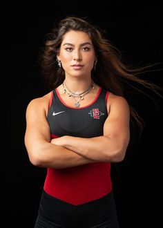 a woman posing with her arms crossed in front of black background wearing a red and black tank top