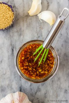 garlic and chili sauce in a glass jar with green onions next to it on a marble countertop