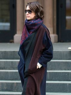 a woman walking down the street with her hand on her hip wearing sunglasses and a scarf