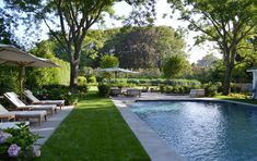 an outdoor swimming pool with lawn chairs and umbrellas next to it, surrounded by trees