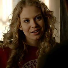 a woman with curly hair and blue eyes looking at the camera while talking to someone