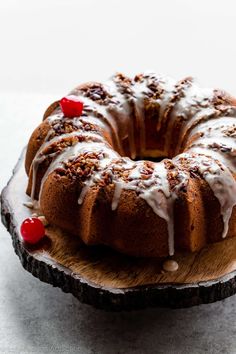 a bundt cake with white icing and cherries on a wooden platter