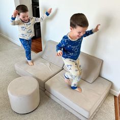 two young boys jumping on top of couches in the living room, one is wearing blue and white pajamas