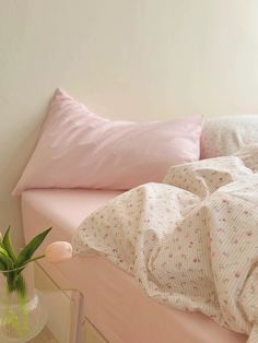 a bed with pink sheets and pillows next to a vase with flowers in it on a table