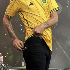 a man in a yellow shirt and black pants on stage with his hands behind his back