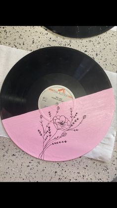 a pink and black vinyl record on a table with a white napkin around it that has a flower drawn on the side