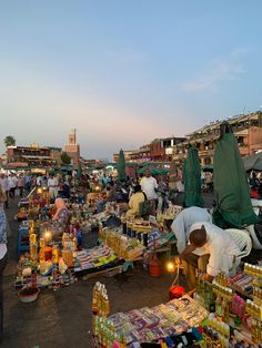 people shopping at an outdoor market in the evening sun, with tents and tables full of goods