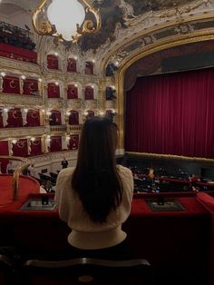 a woman sitting in front of a red curtain on top of a stage with lots of seats