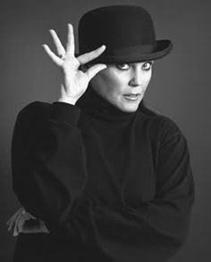 a woman wearing a black top hat and holding her hand up to the side with both hands